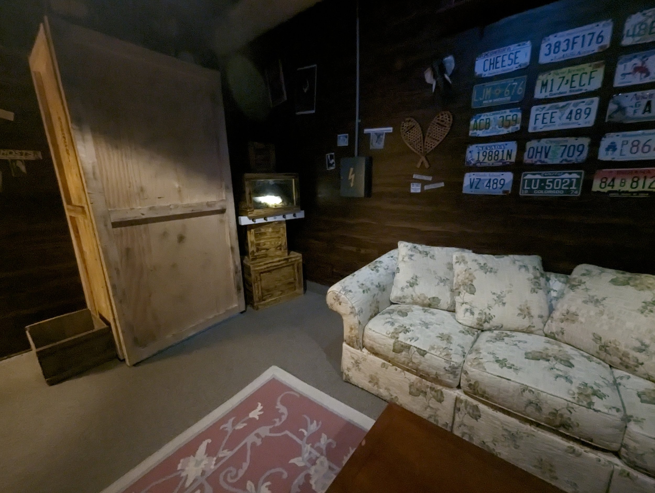 Cozy living room with floral sofa, wooden panel walls, and vintage license plates on the wall.